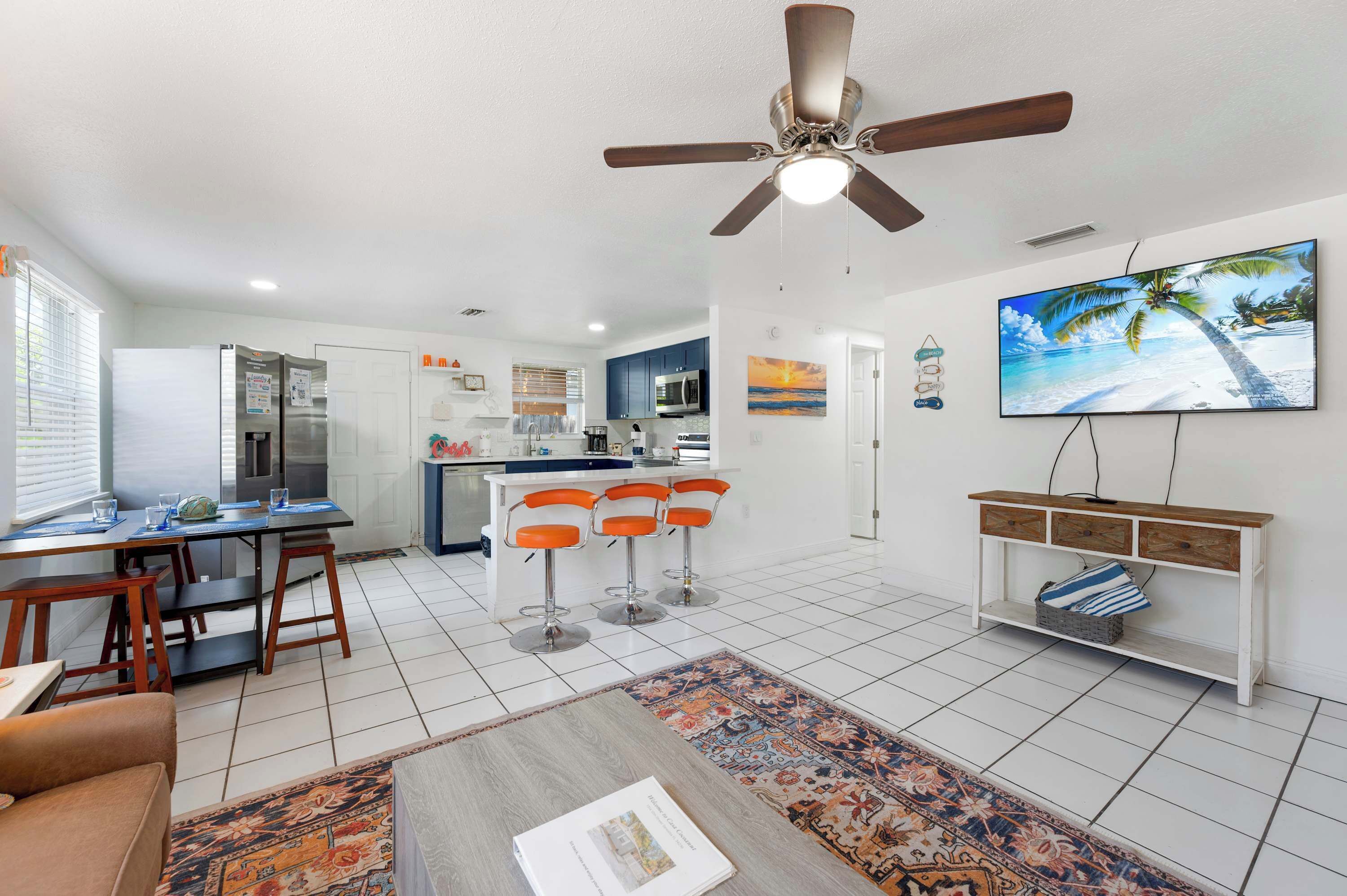 A modern kitchen with a central island, bar stools, a dining table, and a ceiling fan.