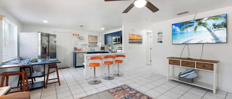 A modern kitchen with a central island, bar stools, a dining table, and a ceiling fan.
