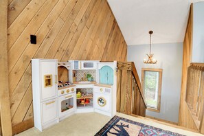 Ein Spielzimmer für Kinder mit Hochbett, einer kleinen Küchenzeile und einem Fenster mit Jalousien.