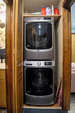 A compact laundry room with two stacked Maytag washing machines and a shelf above containing cleaning supplies. - Hot Tub, EV charger, 3 bedroom, Game room, Renovated Kitchen, 4 min to slopes (Wintergreen Resort)