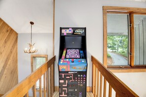 Eine Treppe mit Holzgeländern, eine Kristallleuchtre und ein Retro-Spielautomat mit der Aufschrift 'Arcade Up' in einem Raum mit einem Fenster.