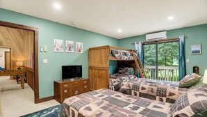 Quarto com duas camas, televisão, guarda-roupa de madeira e janela com vista para árvores.