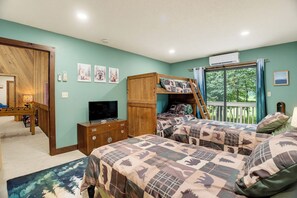 Ein Schlafzimmer mit zwei Betten, einem Fernseher, einem Holzschrank und einem Fenster mit Blick auf Bäume.