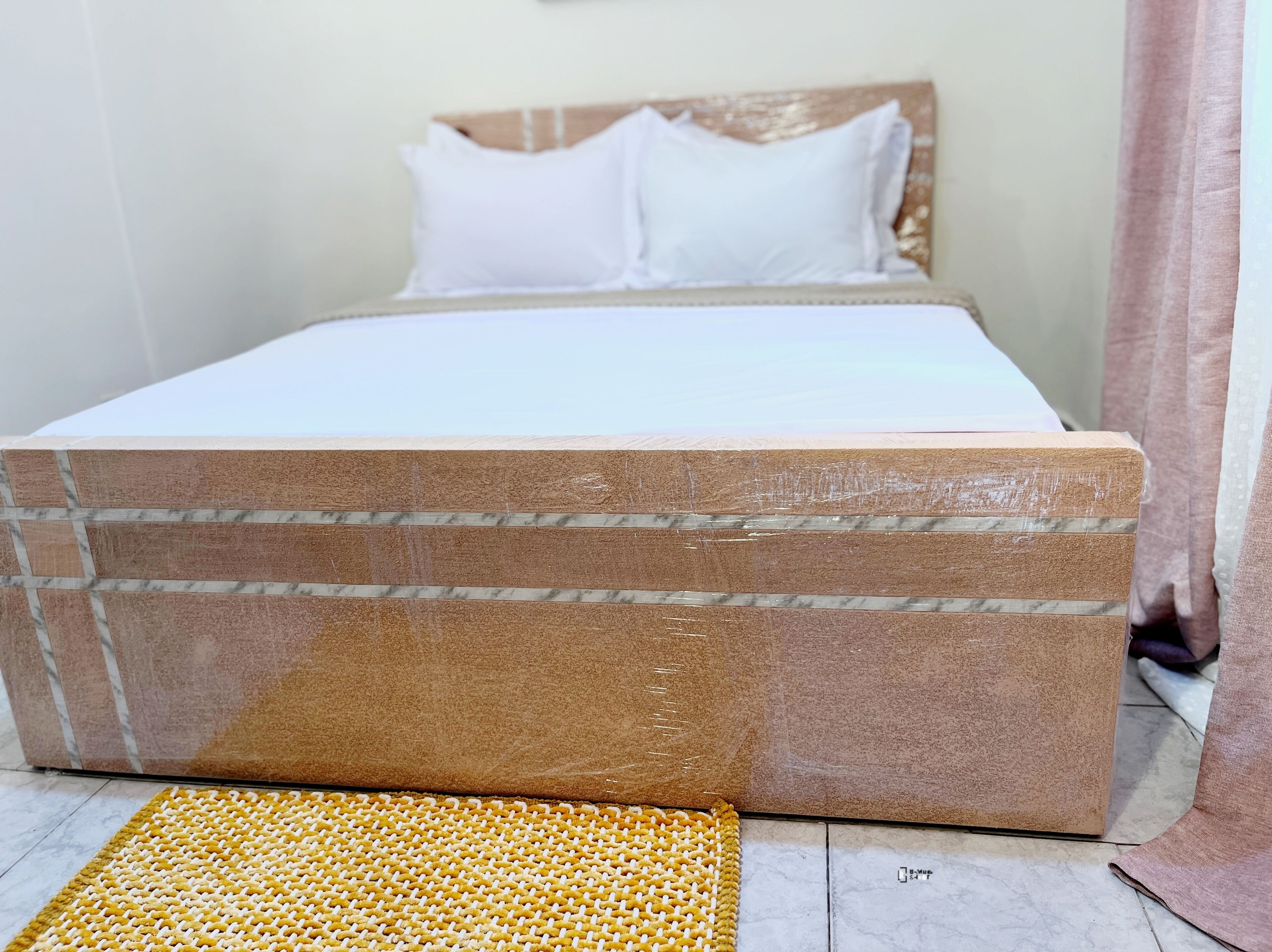 A bed with a wooden headboard, white bedding, and a yellow woven mat on the floor.