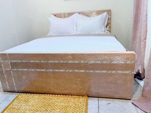 Ein Bett mit Holz-Kopfteil, weißer Bettwäsche und einer gelben gewebten Matte auf dem Boden.