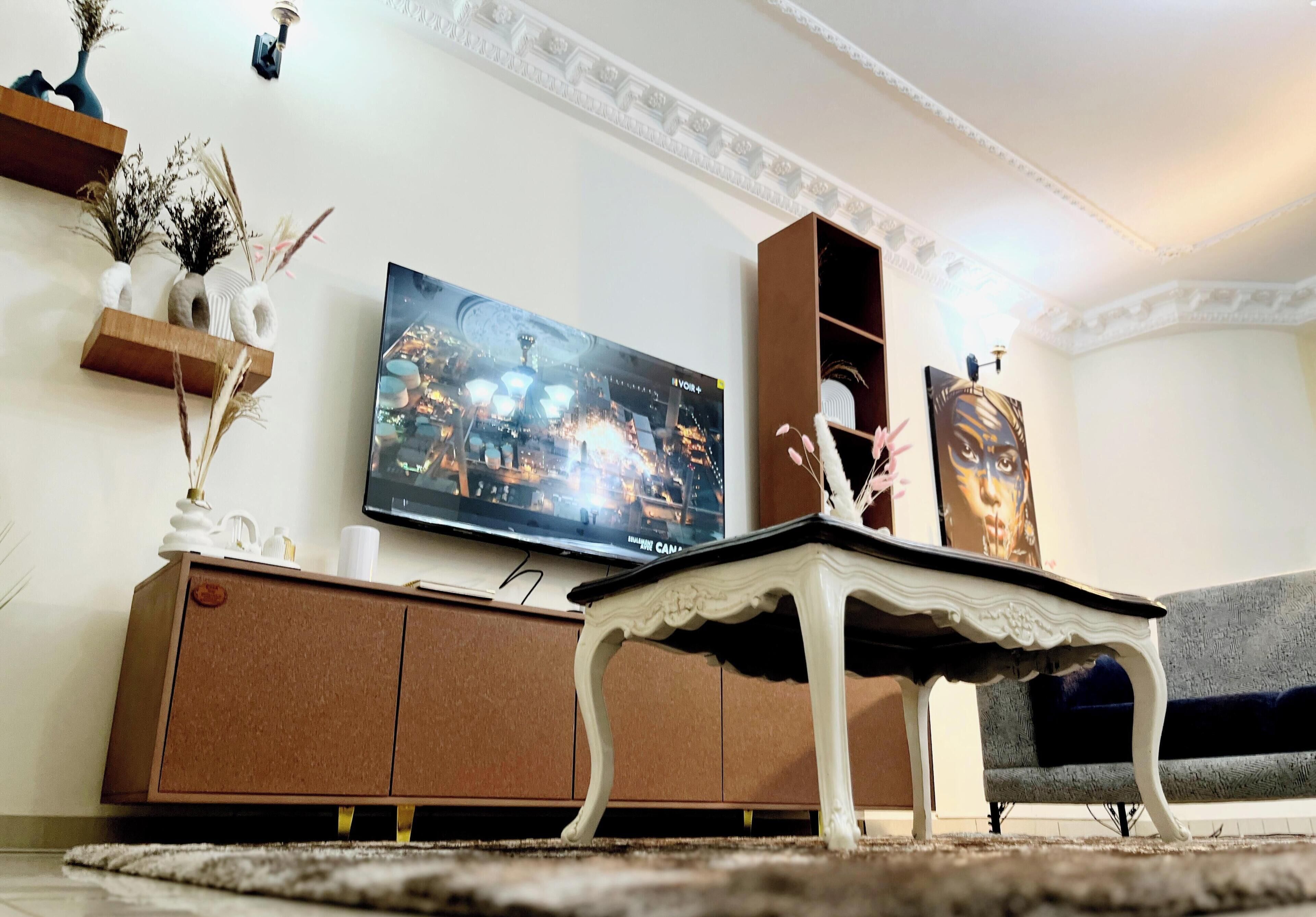 Un salon avec un téléviseur à écran plat fixé au mur, un meuble brun, une table basse blanche et un canapé.