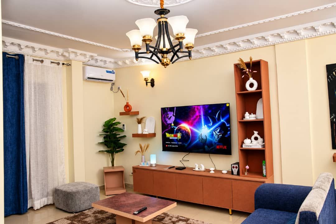 A living room with a flat-screen TV, a sofa, a coffee table, a chandelier, and a plant.