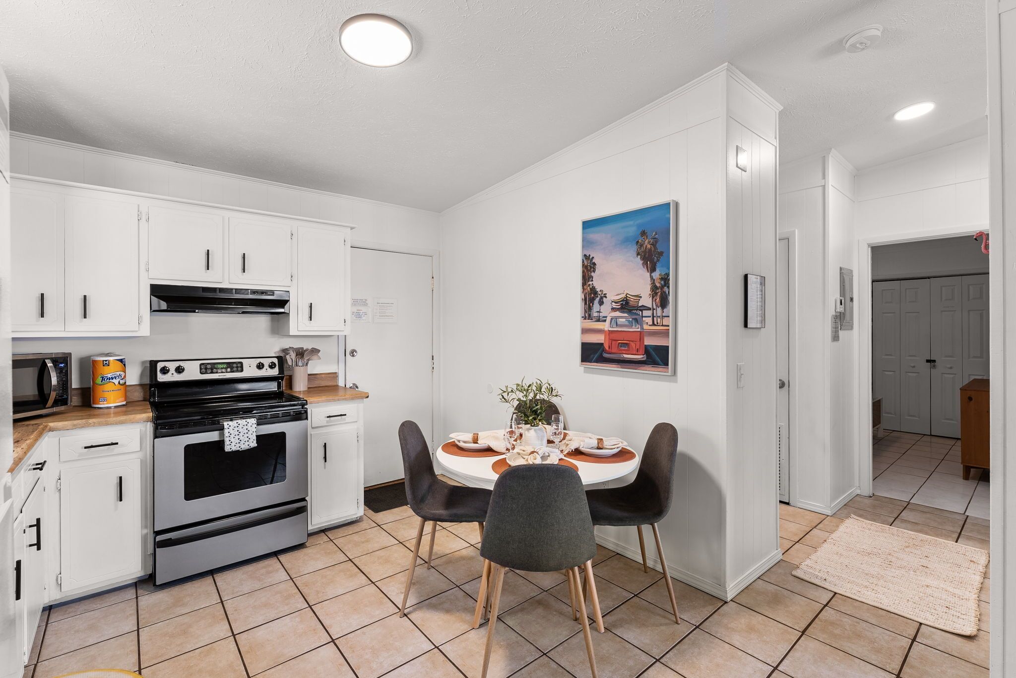 A compact kitchen with white cabinets, a stove, and a dining table set for four. - POOL/Golf Cart/Hot Tub/Playground/Grill/Arcades (Panama City)