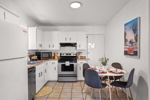 A compact kitchen with white cabinets, a microwave, an oven, and a dining area with a table set for two. - POOL/Golf Cart/Hot Tub/Playground/Grill/Arcades (Panama City)