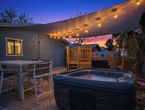 Ein Garten mit Whirlpool, einer Holzterrasse und Lichterketten.