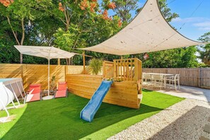 A backyard with a wooden play structure, a slide, a table, and chairs. - POOL/Golf Cart/Hot Tub/Playground/Grill/Arcades (Panama City)