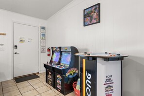 A room with two arcade machines, a ping pong table, and a door with a fire extinguisher. - POOL/Golf Cart/Hot Tub/Playground/Grill/Arcades (Panama City)