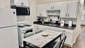 A modern kitchen with white cabinetry, a built-in microwave, a gas stove, and a marble-top dining table with two chairs.