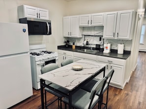 A modern kitchen with white cabinetry, a built-in microwave, a gas stove, and a marble-top dining table with two chairs.