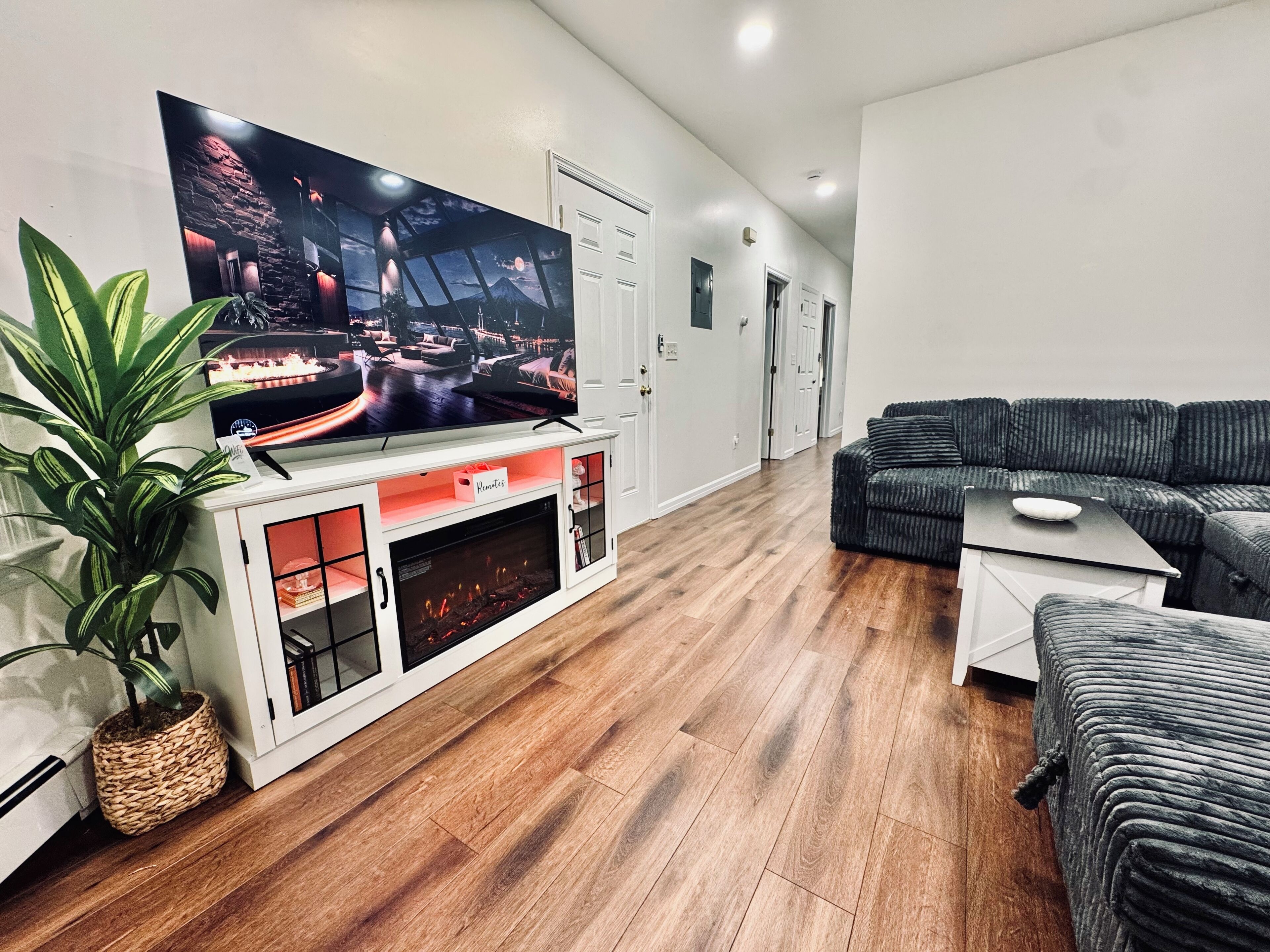 A modern living room with a flat-screen TV, a fireplace, a grey sofa, and a potted plant.