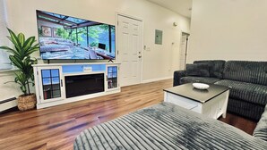 A living room with a flat-screen TV, a sofa, a coffee table, and a potted plant.