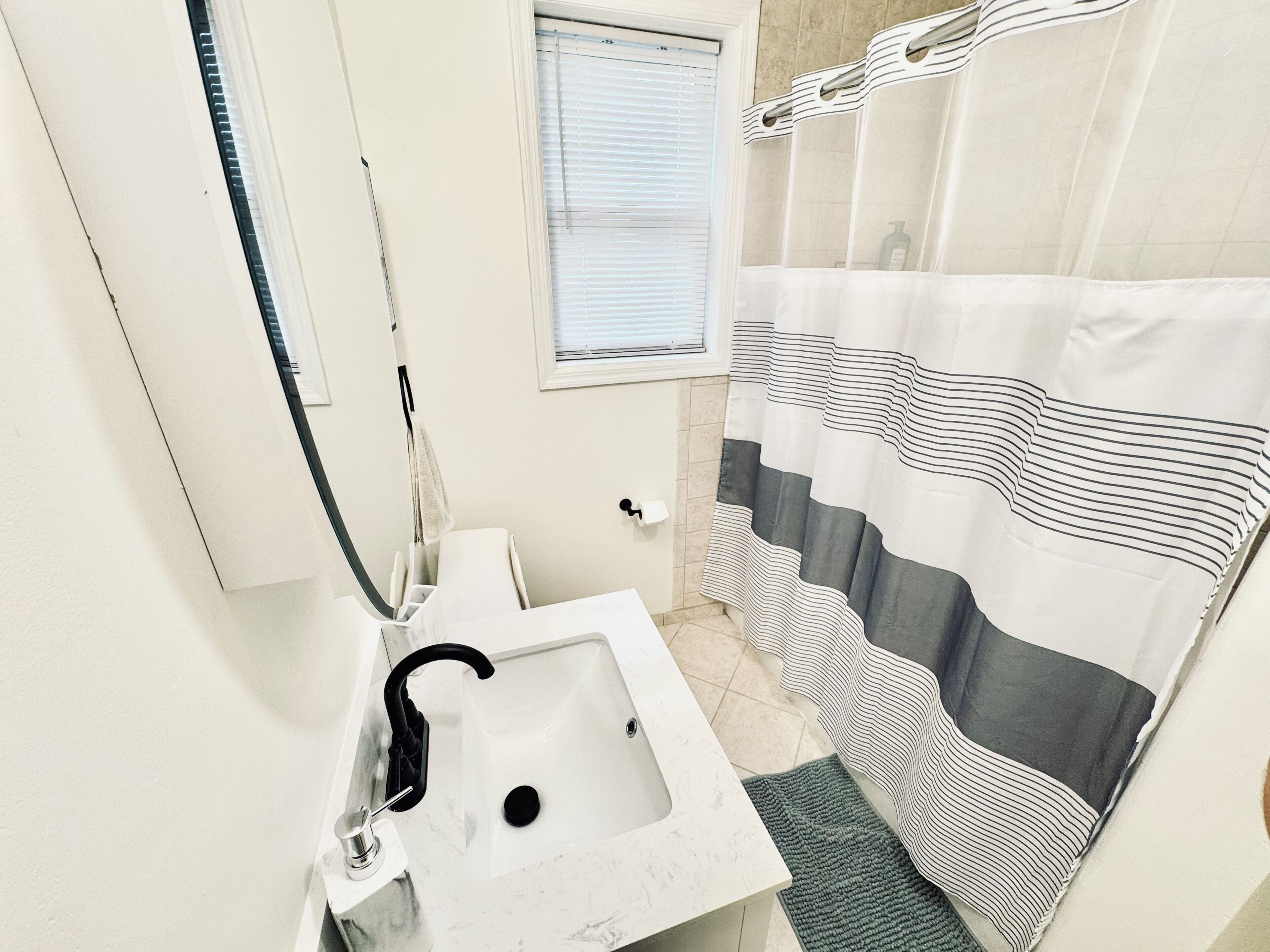 A bathroom with a white sink, a mirror, a window, and a striped shower curtain.
