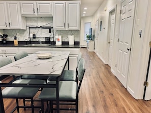 A modern kitchen with white cabinets, a marble countertop, and a dining area with a table and chairs. - Luxe, Bright & Stylish 2Bed Unit w/Parking near NYC! (Haledon)
