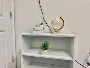 A white shelf with a globe, a box labeled 'Remotes,' and a small plant. - Luxe, Bright & Stylish 2Bed Unit w/Parking near NYC! (Haledon)
