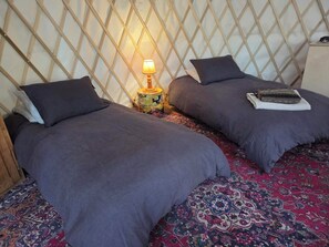 A room with two beds, a patterned carpet, a wooden lattice wall, and a small table with a lamp.