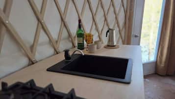 Un coin cuisine équipé d’une cuisinière à gaz, d’un évier, d’une machine à café et d’une bouteille d’alcool posée sur le comptoir.