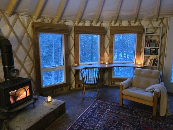 A cozy interior with a wood-burning stove, a chair, a desk with a chair, and a bookshelf.