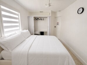 Ein Schlafzimmer mit Bett, Kleiderschrank mit Kleidung, einer Wanduhr und einem Deckenventilator.