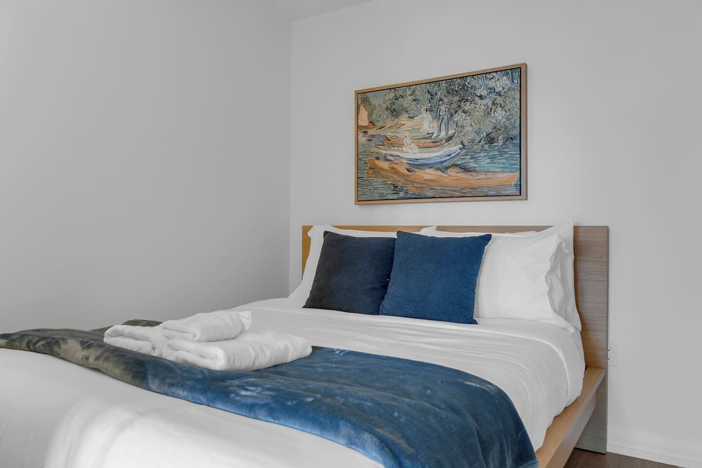 A bedroom with a bed, pillows, a blanket, and a painting on the wall.