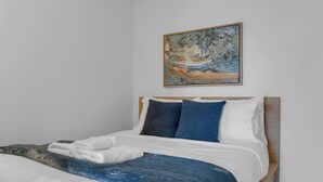 Ein Schlafzimmer mit einem Bett, Kissen, einer Decke und einem Bild an der Wand.