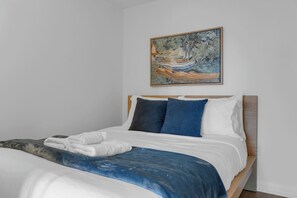 Ein Schlafzimmer mit einem Bett, Kissen, einer Decke und einem Bild an der Wand.