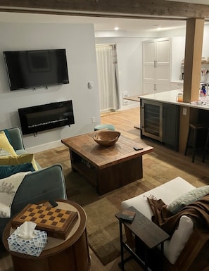 A living room with a television, a coffee table, a sofa, and a small table with a chessboard.