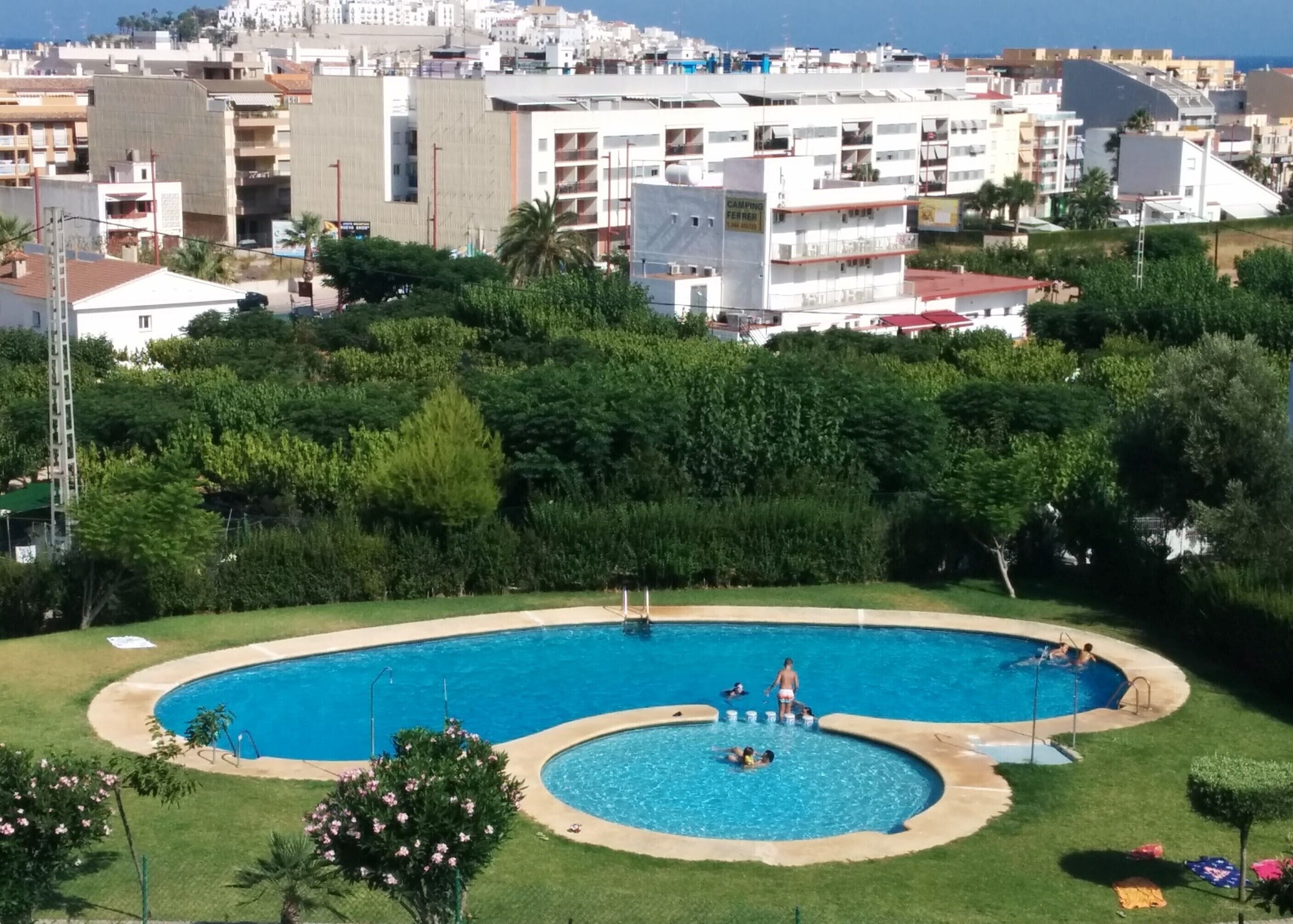 A residential area with a swimming pool surrounded by greenery and a view of a coastal cityscape.