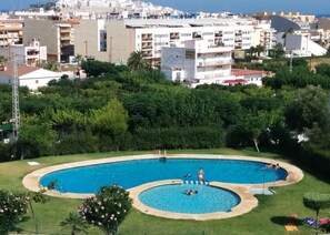 Et boligområde med en swimmingpool omgivet af grønt og udsigt til en kystby.