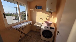 Ein kleiner Hauswirtschaftsraum mit Waschmaschine, Spüle und Bügelbrett neben einem Fenster.
