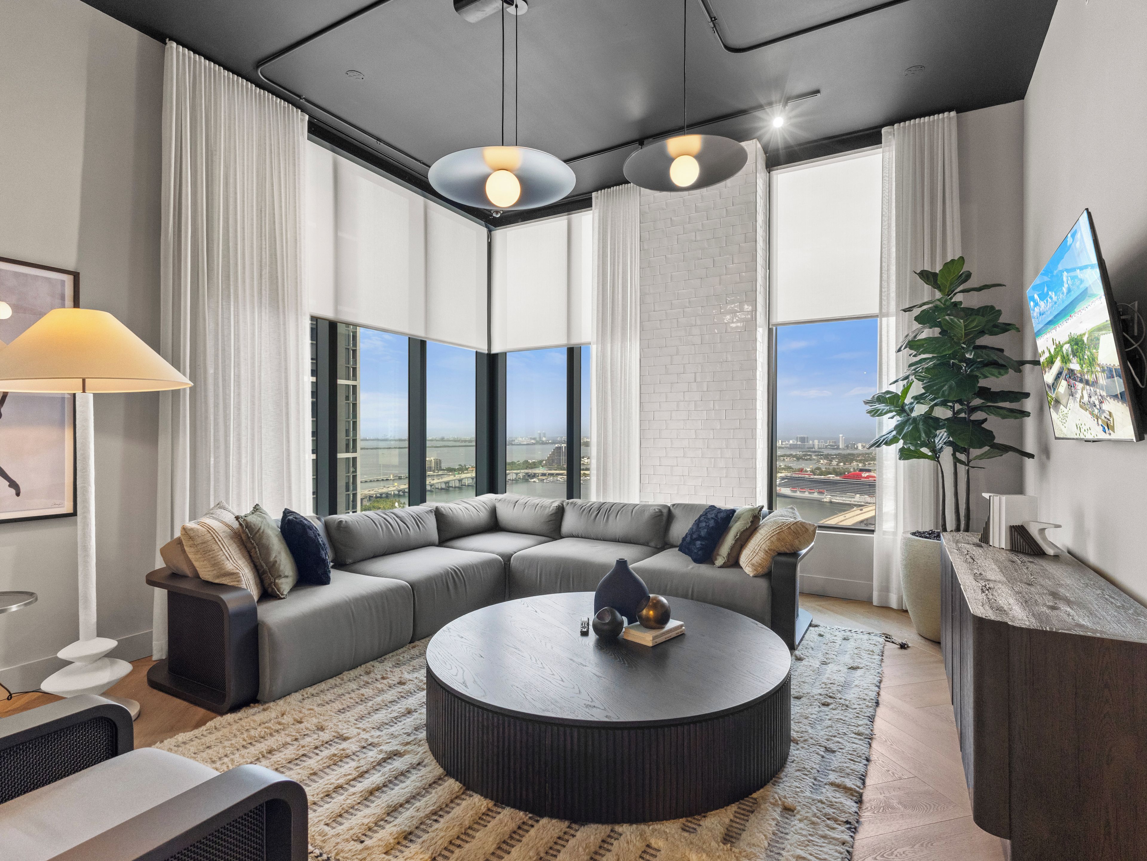 A modern living room with a sectional sofa, a round coffee table, and large windows offering a city view.