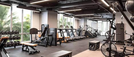 A gym with various exercise equipment, large windows, and a view of greenery outside.