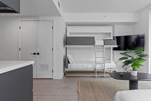 A modern, compact room with a bunk bed, a flat-screen TV, a small table with a plant, and a door. - *NEW* Lux Condo | High-Floor Views · Gym · Pool · (Miami)