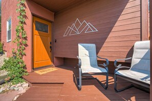 A wooden door with a 'HELLO' mat, two white chairs, and a wall with a geometric design. - Broadmoor Retreat with Hot Tub and a Fire Pit (Colorado Springs)