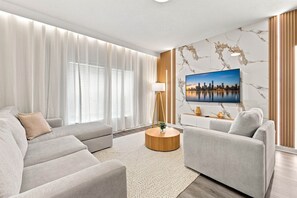 A modern living room with a large flat-screen TV, two sofas, a coffee table, and a marble-patterned wall. - Mickey & Mario Luxury Retreat, private pool (Kissimmee)
