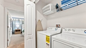 A laundry room with a front-loading washer and dryer, a drying rack, and a wall-mounted ironing board. - Mickey & Mario Luxury Retreat, private pool (Kissimmee)