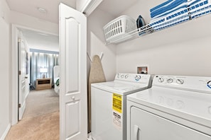 A laundry room with a front-loading washer and dryer, a drying rack, and a wall-mounted ironing board. - Mickey & Mario Luxury Retreat, private pool (Kissimmee)