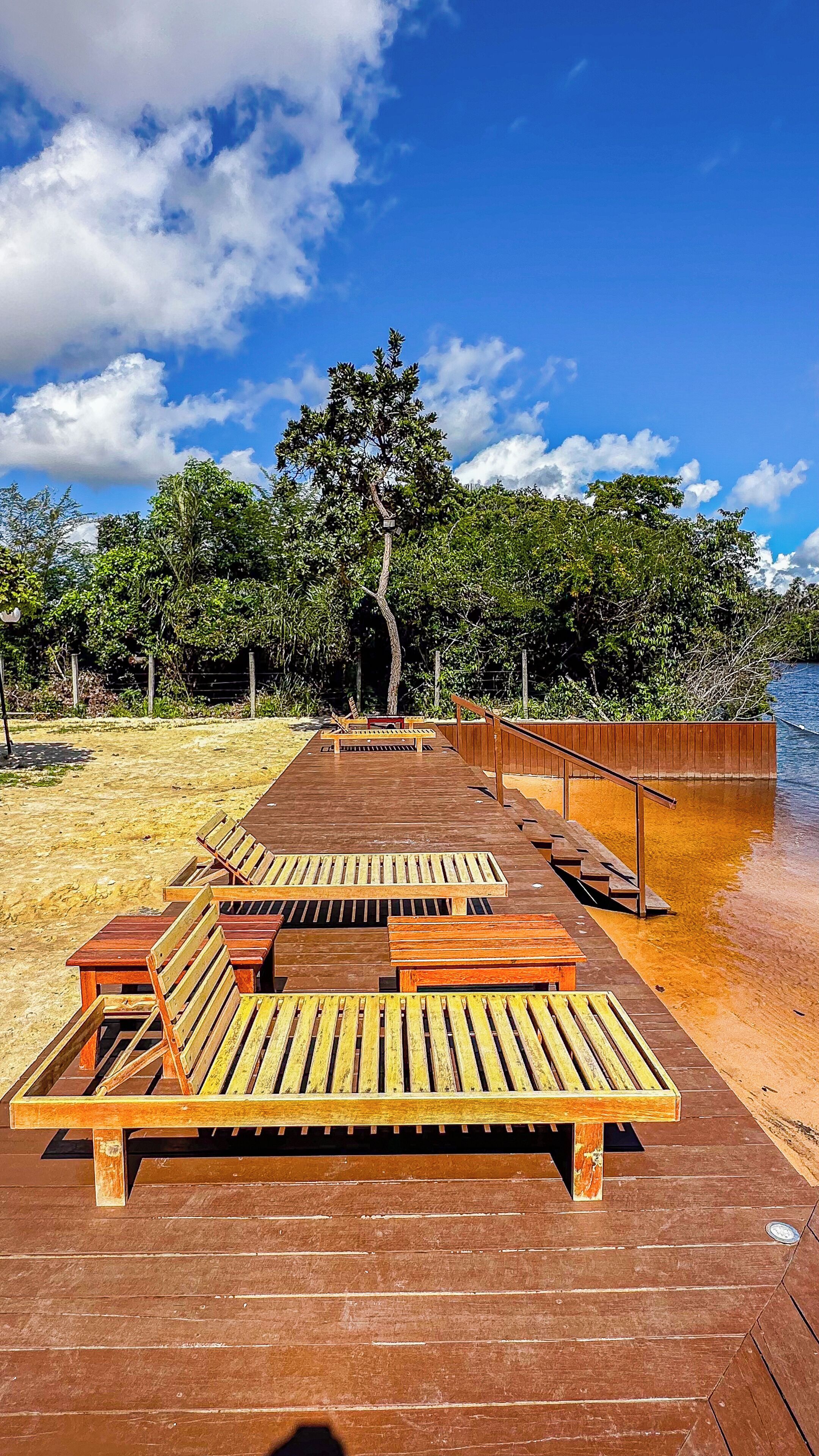 A wooden deck with benches and a railing, leading to a body of water.