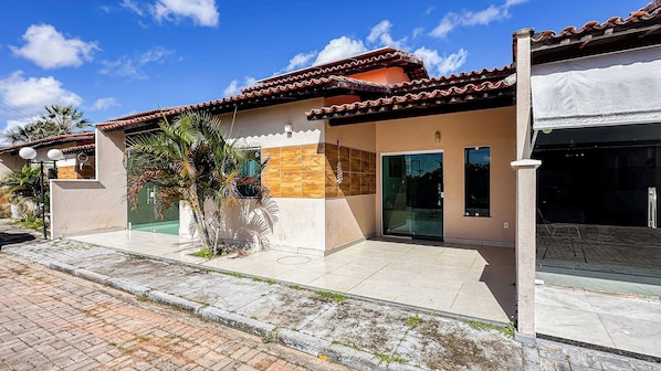 A modern building with a tiled roof, a glass door entrance, and a paved sidewalk. - Casa Summer Ville em Barreirinhas/em condomínio/piscina privativa (Barreirinhas)