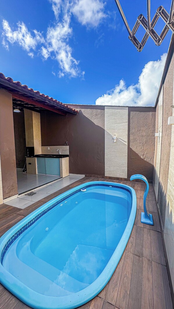 A swimming pool with a tiled deck, a built-in kitchen area, and a stone wall.