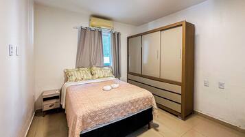 A bedroom with a bed, a nightstand, a wardrobe, and a window with curtains.