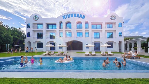 A large building with a swimming pool, multiple windows, and a sign that reads 'NINHVANA'. - Ninhvana Oceanfront Resort (Dong Ninh Hoa)