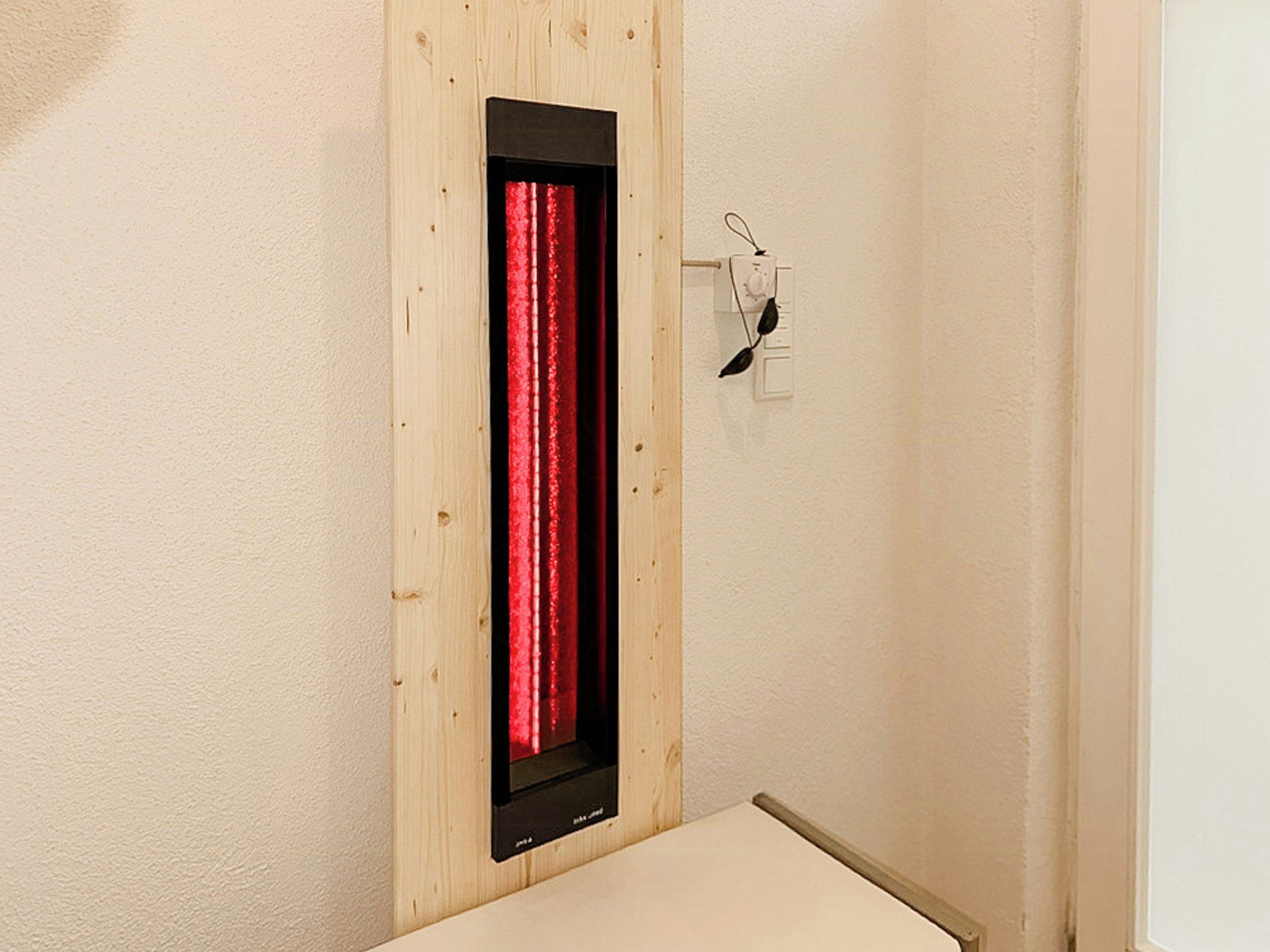 A room with a wooden panel wall, a red curtain, and a small shelf with a pair of glasses.
