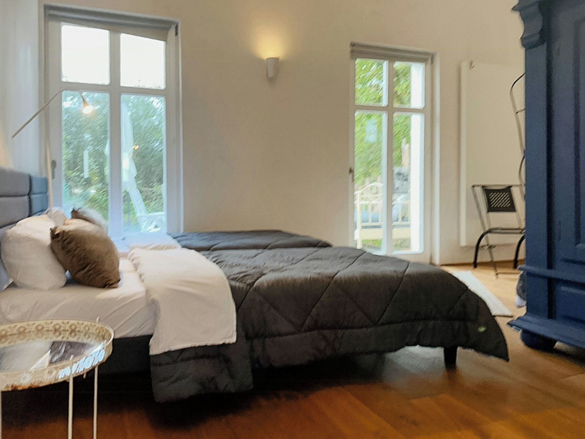 Ein Schlafzimmer mit einem Bett, zwei Fenstern, einem Sessel und einem Tisch.