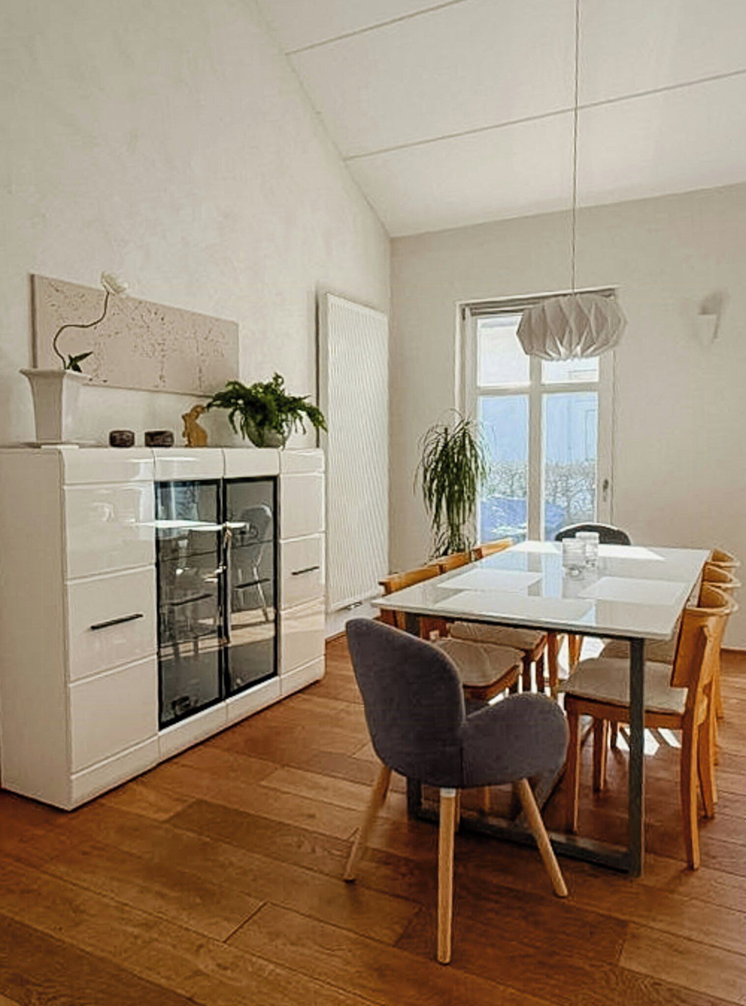 A modern kitchen with white cabinetry, a glass-fronted refrigerator, and a dining area with a wooden table and chairs.