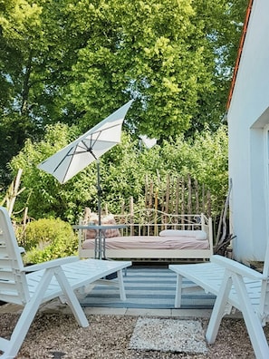 A patio with a bed, white chairs, and a large umbrella.